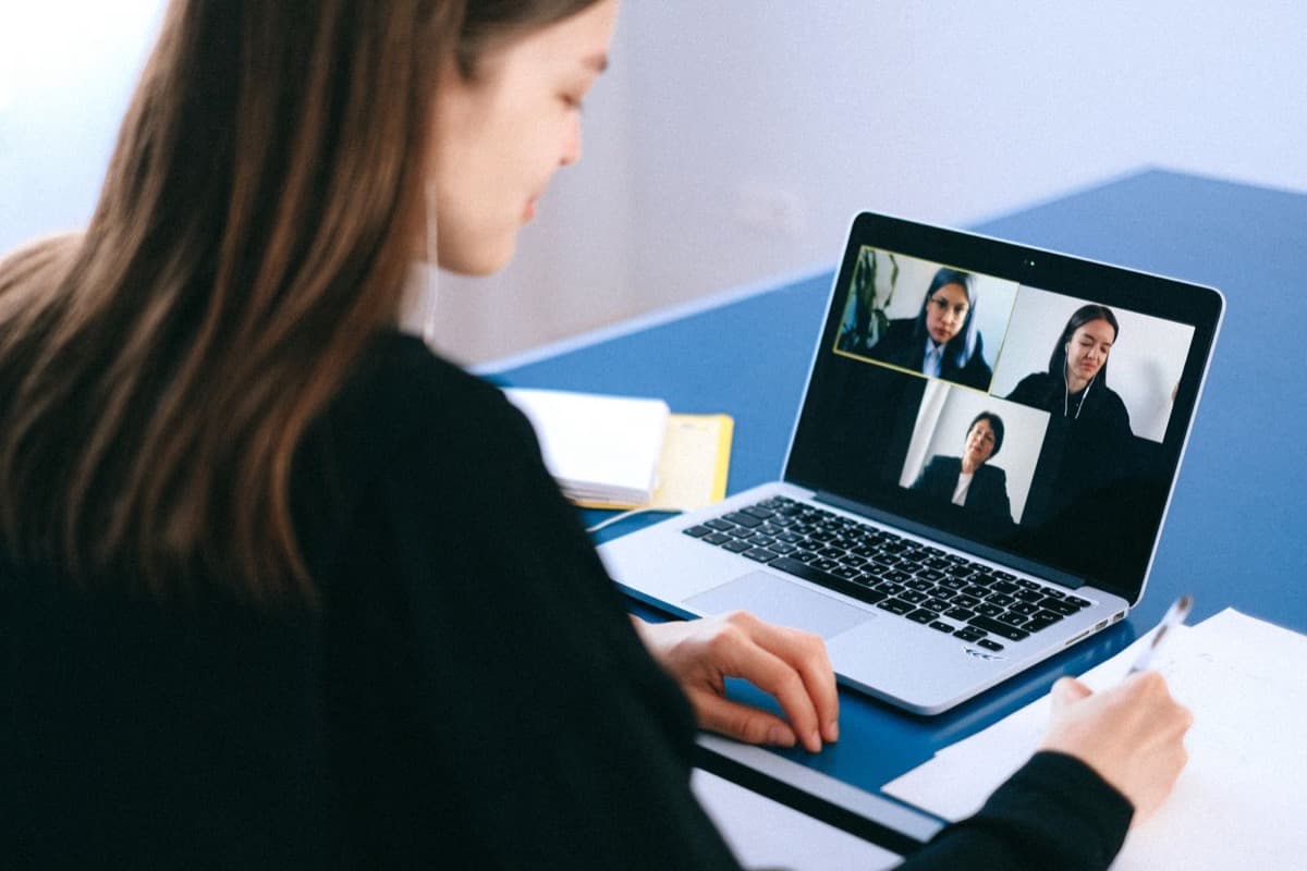 Laptop open to a video call with documents arranged beside it on a bright desk